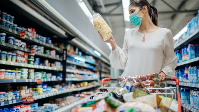 Young person with protective face mask buying groceries/supplies in the supermarket.Preparation for a pandemic quarantine due to coronavirus covid-19 outbreak.Choosing nonperishable food essentials